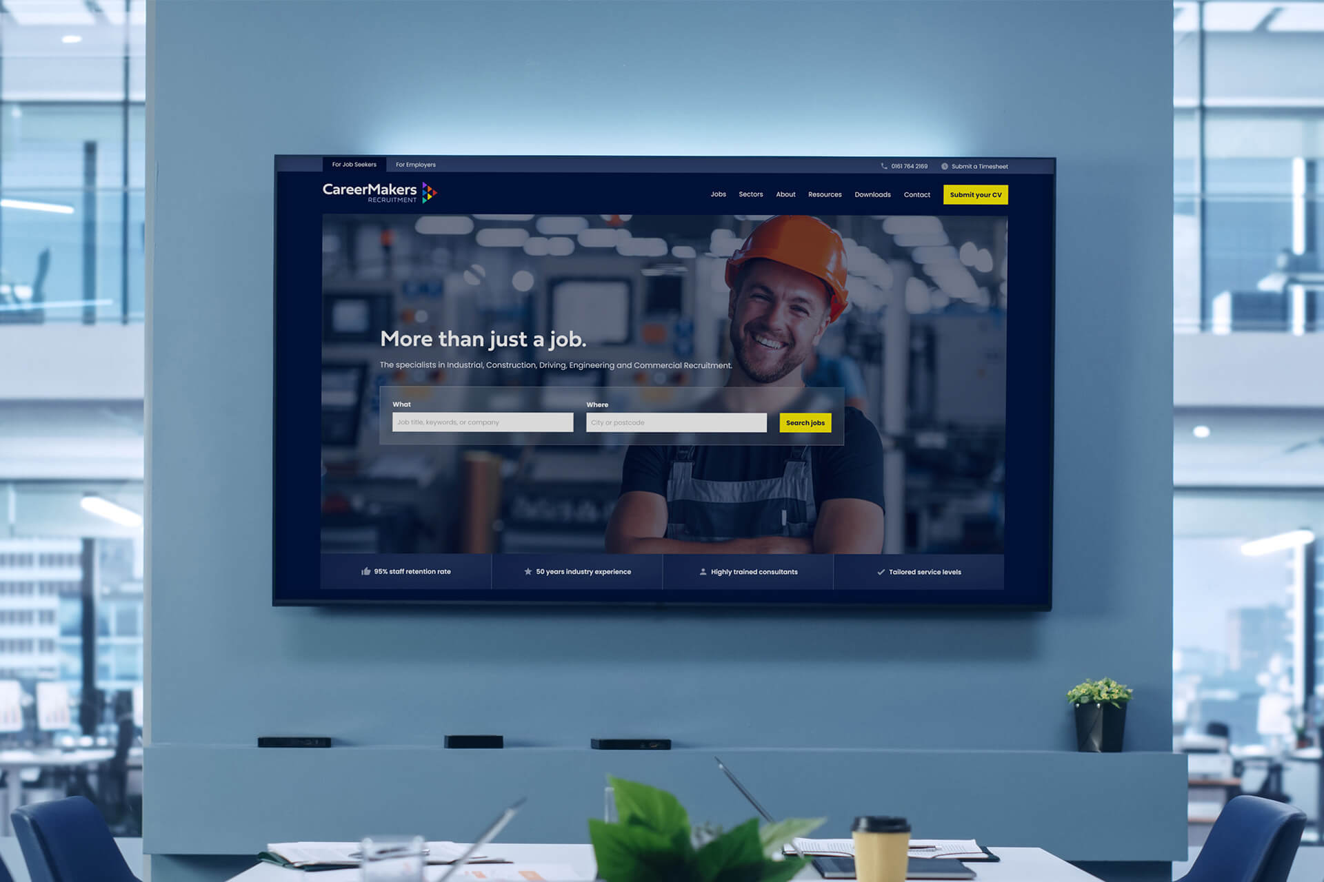 A mockup of a website homepage displayed on a large screen in a modern office meeting room.